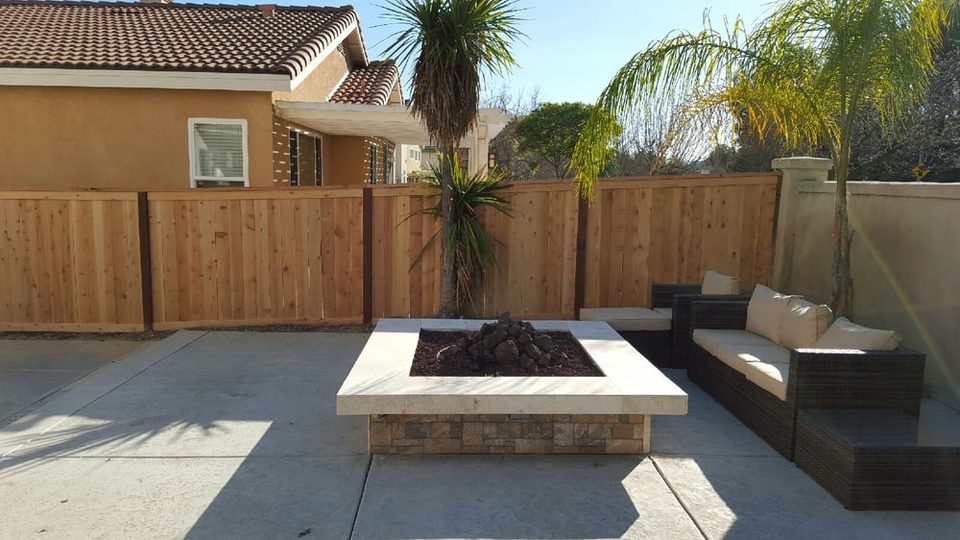 Wood fence enclosing a backyard patio with a fire pit and lounge seating