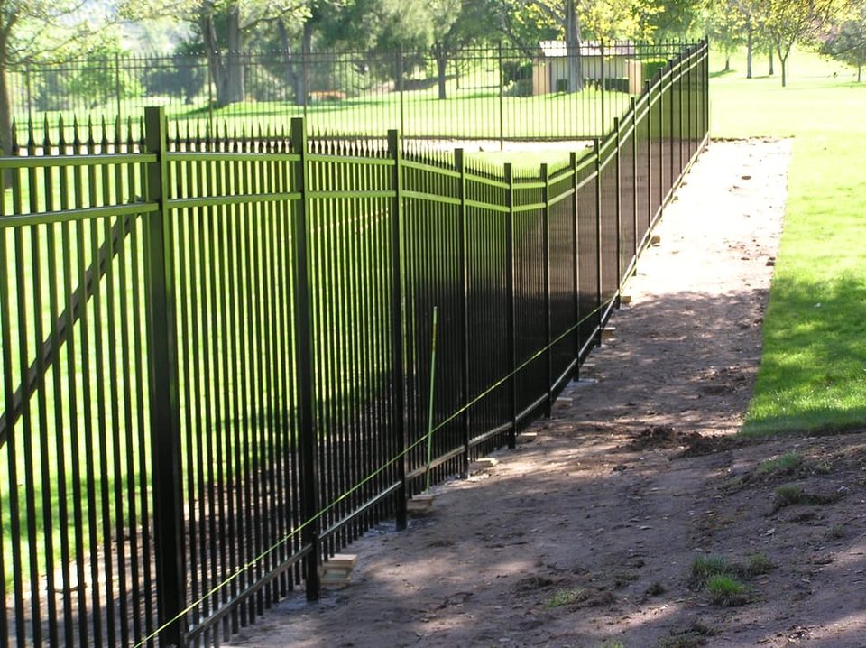 Black iron fence stepped down a slope beside an open green