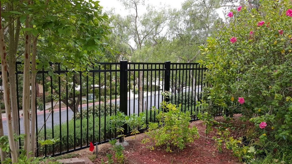 Black ornamental iron fence bordering a mature flowering garden