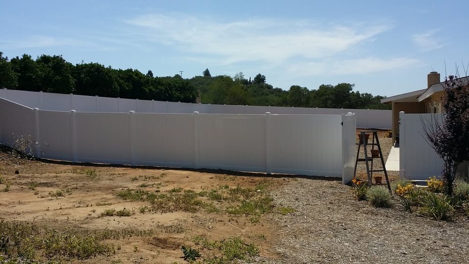 Long white vinyl privacy fence enclosing a rural back lot
