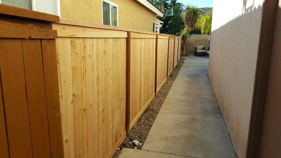 Tall wood privacy fence along a concrete side-yard walkway